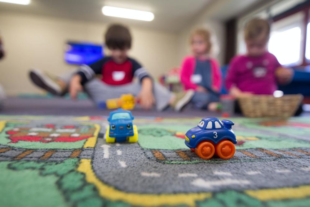 students playing with cars on a road rug 